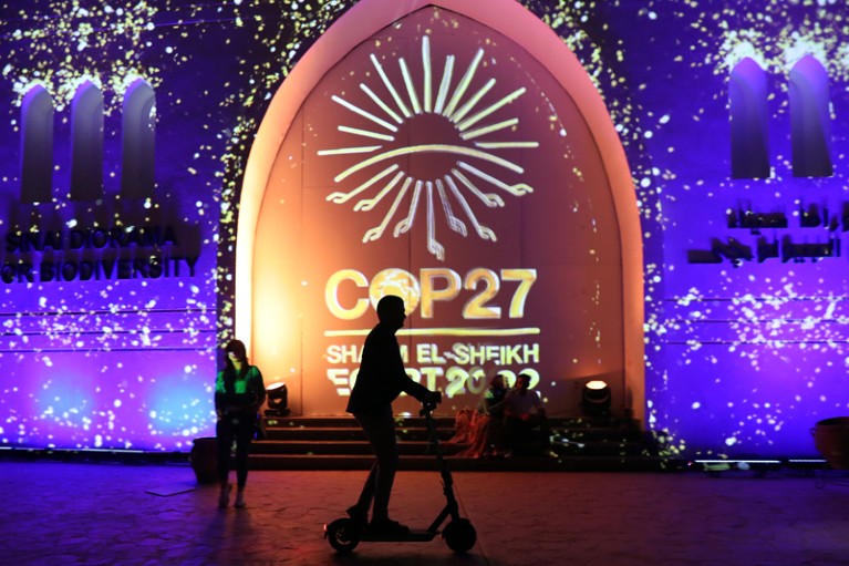The silhouette of a person on an electric scooter rides in front of a projected COP27 logo