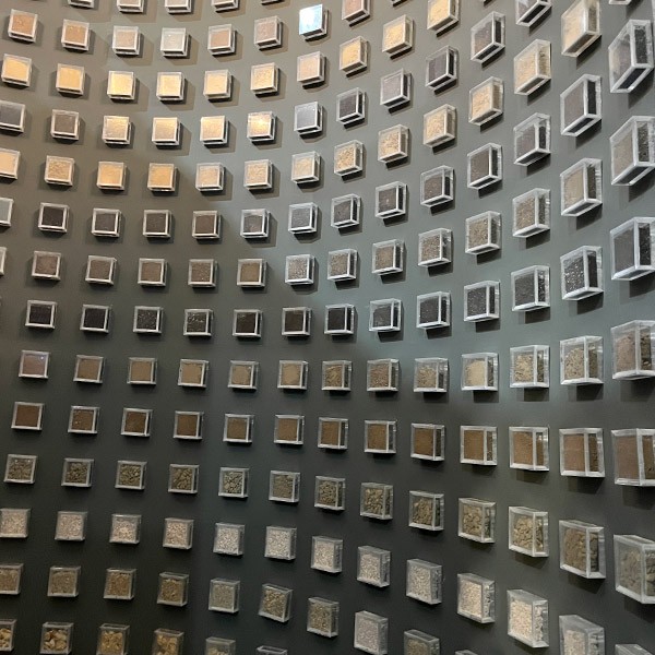 A curving grey wall studded with rows of clear cubes, all filled with different colours of soil.