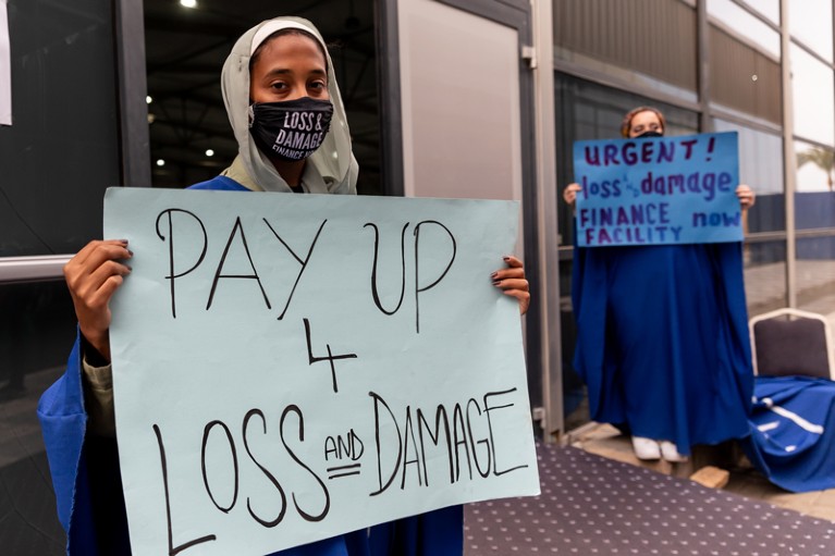 Women activists wearing face masks hold signs demanding Loss and Damage funding