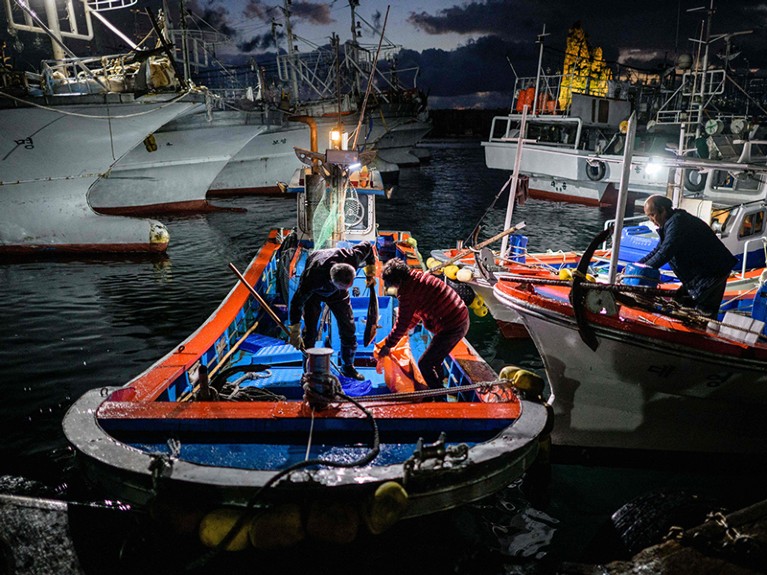 Dos personas en un bote pequeño ponen un pescado recién capturado en una bolsa de plástico.