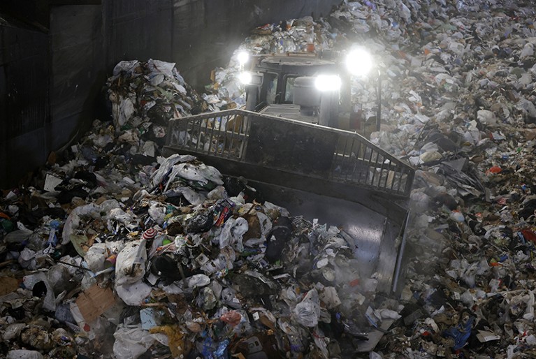 A bulldozer with a bright headlight pushes a pile of trash in a pit at Recology in San Francisco, California in 2021.