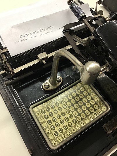 The Mignon 3 index typewriter with type on a white piece of paper in the platen fed into the typewriter's carriage.