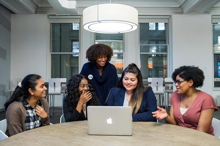 CEO Tarika Barrett with college students gathered around a Macbook computer.