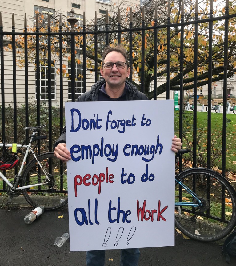 Rob Thomas holds a sign reading 'Don't forget to employ enough people to do all the work!!!'