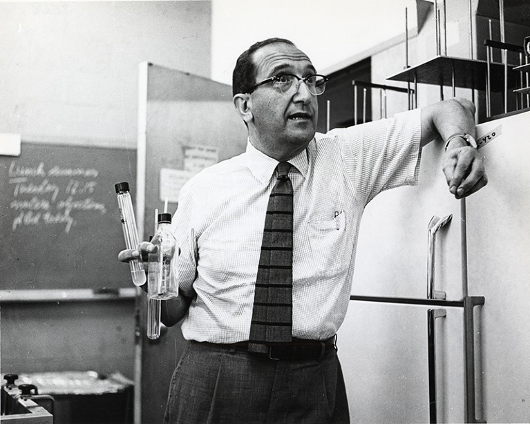 Salvador Edward Luria, an Italian microbiologist, holding test tubes in a lab area with refrigerators.
