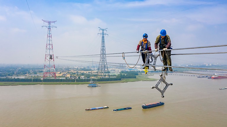 Two workers install electric wires on the 385-meter-high world's tallest transmission tower by the side of Yangtze River
