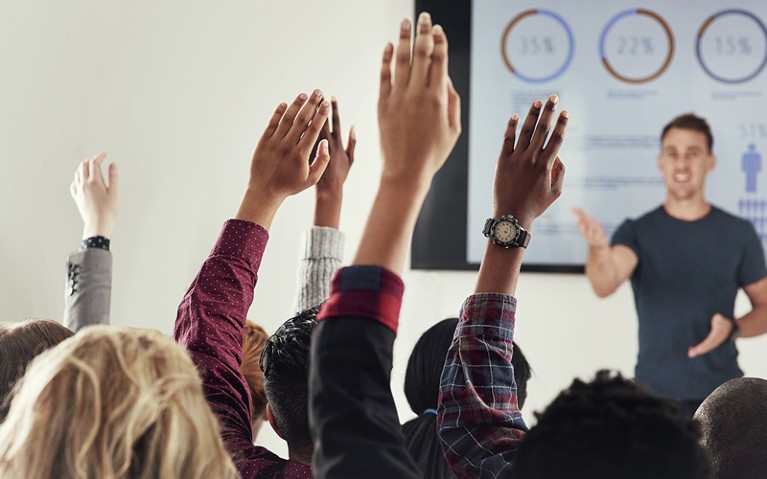 Cropped shot of a group of people raising their hands in a class.