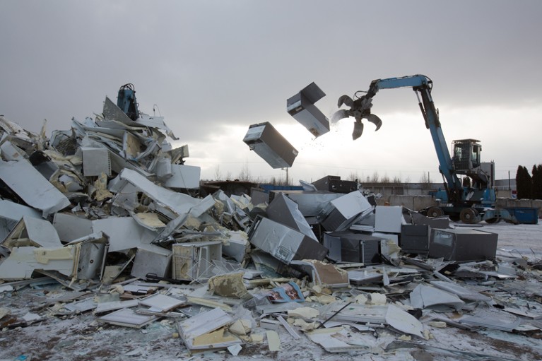 A claw crane tosses scrapped refrigerators on a dark and snowy day