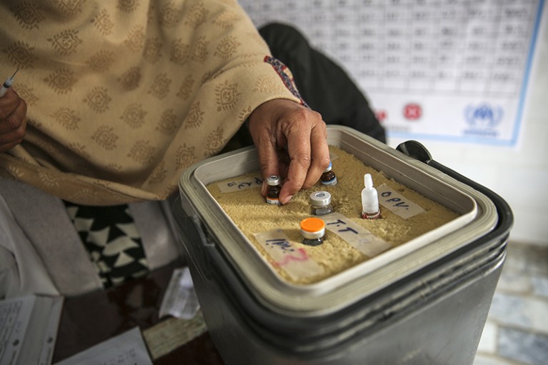 Close-up of a box containing vaccines with a hand reaching for a vial.