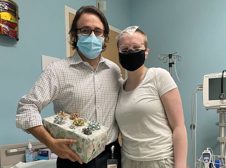 Emily in hospital wearing a black face mask standing next to Nicholas Vitanza holding a Christmas present.