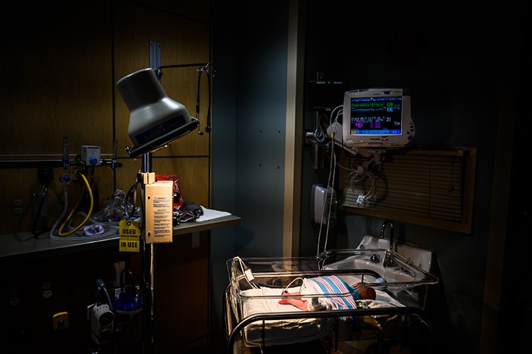 Dimly lit hospital room with a newborn baby lying in an incubator. Above him, a screen shows his vital signs.