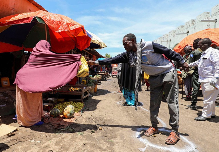 A Somali woman in a Mogadishu market sells fruits to a customer standing on social distancing marker