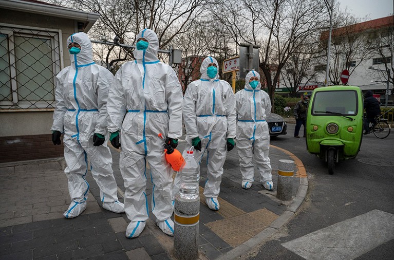 Epidemic control workers wearing protective clothing wait to enter a lockdown area.