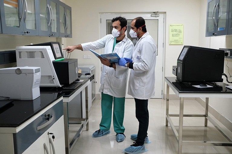 在新德里的新冠病毒基因组测序实验室内，技术人员正在讨论一台台式测序仪，同时测试样本