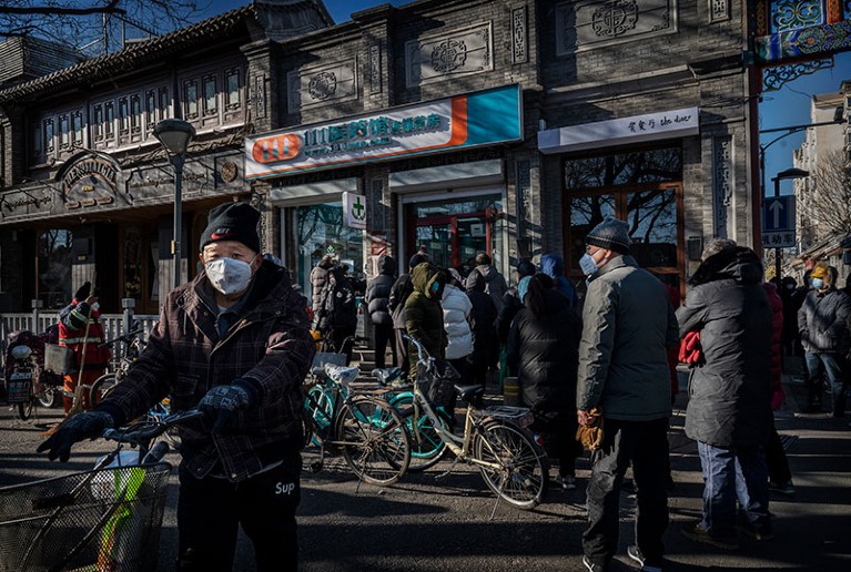 People in masks, coats and hats gather outside a shop.