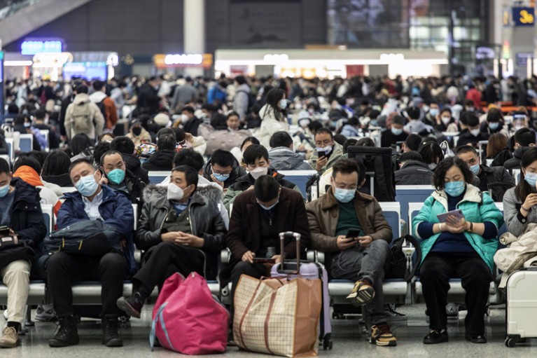 在上海虹桥火车站，戴着口罩的旅客们拿着行李坐在一排排的椅子上