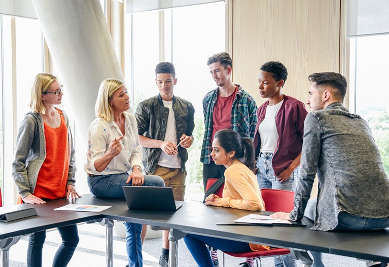 Casual students with female teacher in modern college building, woman in her 50s explaining to young people in their 20s.