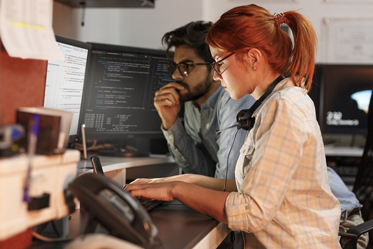 Two programmers working on a project examine a computer screen of code.