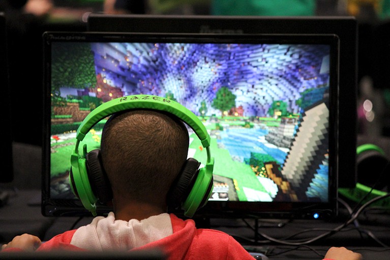 A child with headphones on in front of a monitor, plays the video game Minecraft at the Minecon convention in London, 2015.