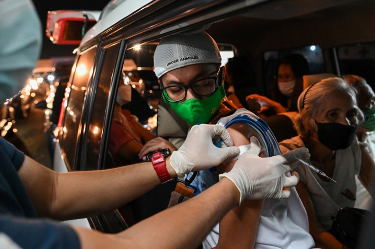 A health worker puts on an adhesive bandage after inoculating a man wearing a green face mask in his car