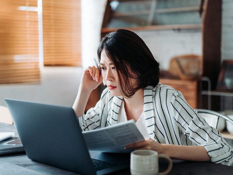 Young Asian woman handling home finances with laptop.