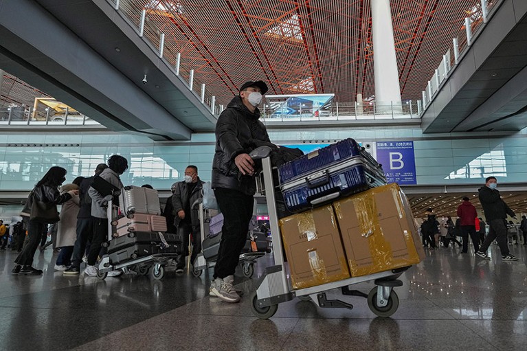 People with masks moving luggage in an airport.