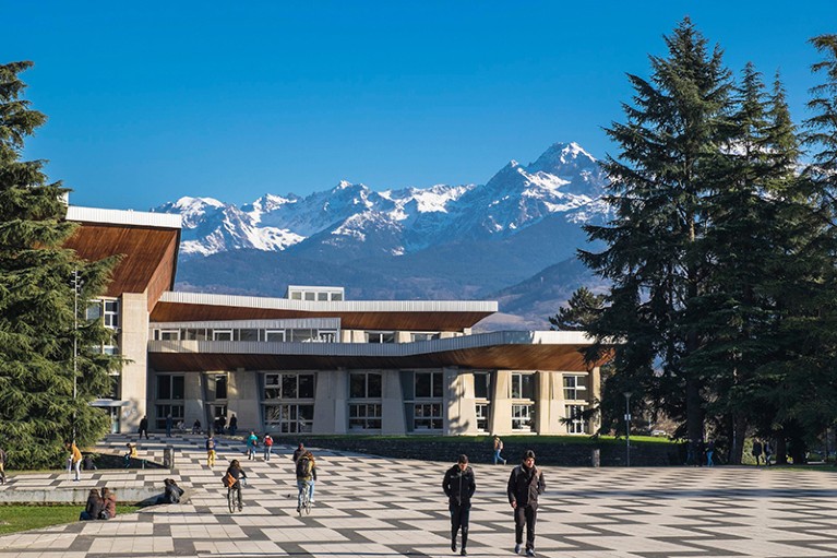 People walk in front of the campus of Grenoble Alpes University, mountains in the background