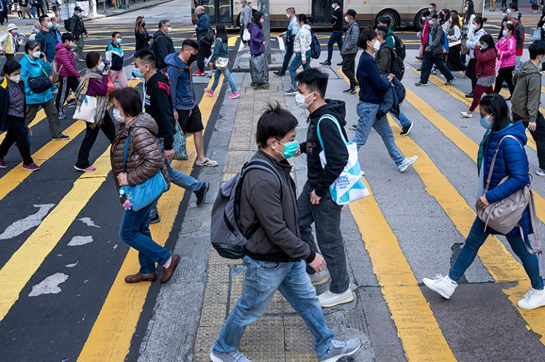 Pedestrians wearing face masks walking across a busy zebra crossing junction in Hong Kong