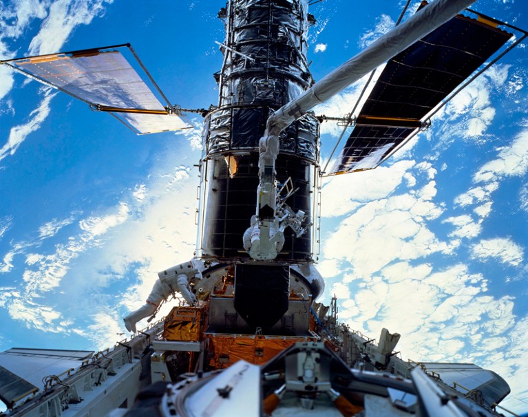 Astronauts servicing the Hubble Space Telescope over Earth