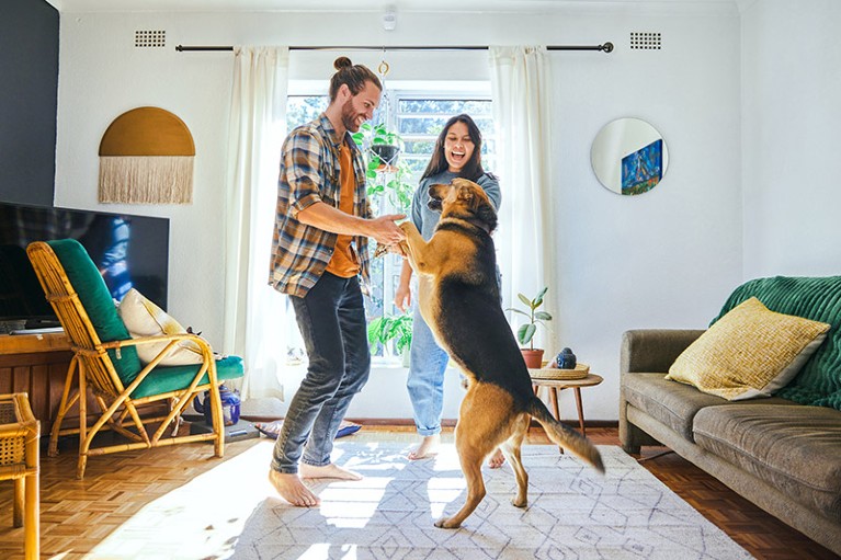 A young couple dancing in the living room with their pet dog