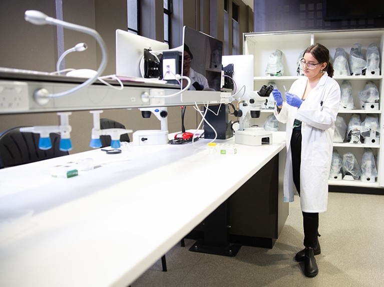 Woman in lab coat pipetting at a bench.