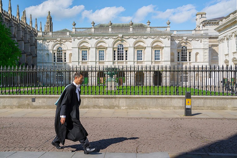 英国剑桥，一名穿着学院长袍的大学生走过国王游行区的大学老校舍
