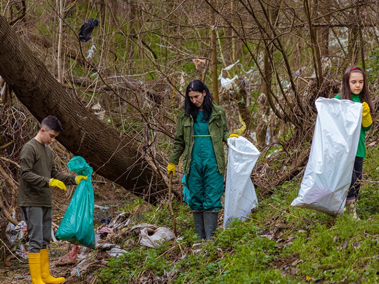 Caring Caucasian family, mother with her son and daughter, cleaning the garbage from river and in the forest.