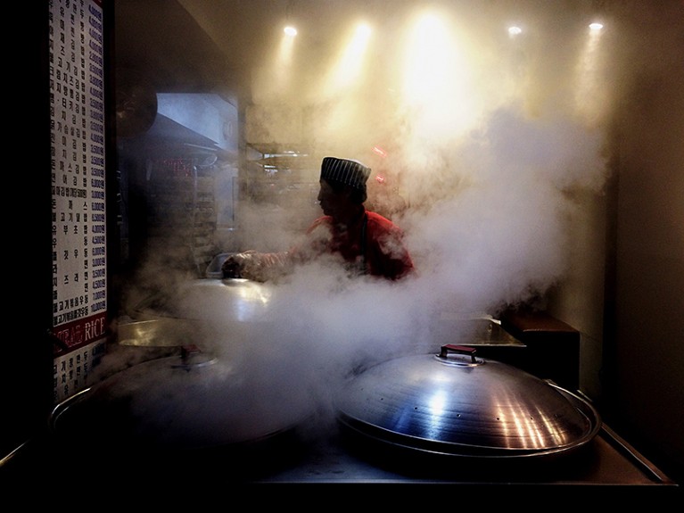 一位厨师在餐厅里做饭，烟雾和蒸汽在他们周围翻滚。