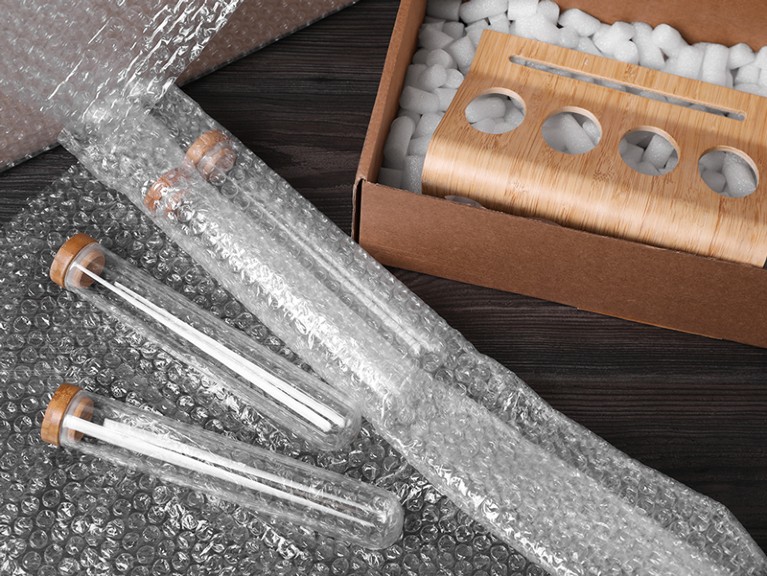 Test tubes with bubble wrap and cardboard box on dark wooden table.