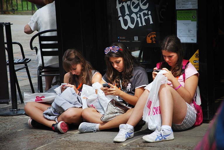 Three teenage girls checking their mobile phones in Canterbury Town center, UK.