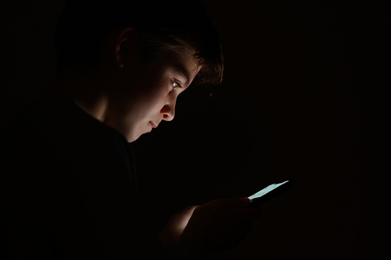 A teenage child looks at the screen of a mobile phone while in the dark