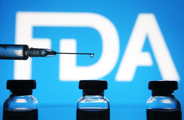 A medical syringe and vials are seen in front of the Food and Drug Administration (FDA) logo