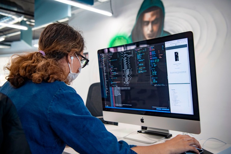 Over-the-shoulder view of a student wearing a face mask using a computer in a lab room.