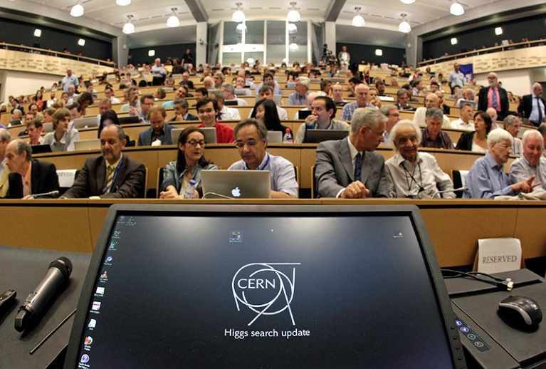 从讲台上看到一个完整的演讲厅，电脑显示器上显示着“希格斯粒子搜索更新”字样。