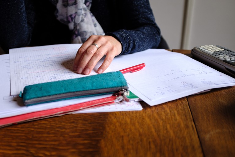 Close-up of a woman sitting at a wooden table with papers, a red pen and a calculator