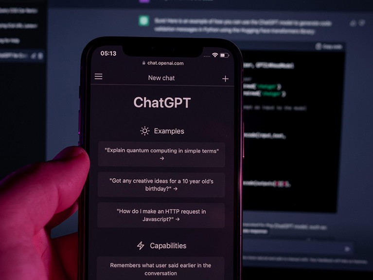 用户手持带有ChatGPT服务的智能手机，在背景模糊的ChatGPT提示下，在笔记本电脑上进行代码编程。