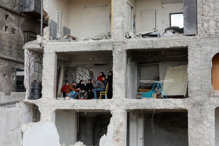 A family sit in their home which has been destroyed by the earthquake