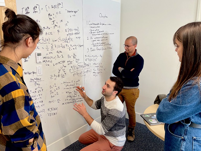 Four adults focused on a large white board which is covered with words and equations.