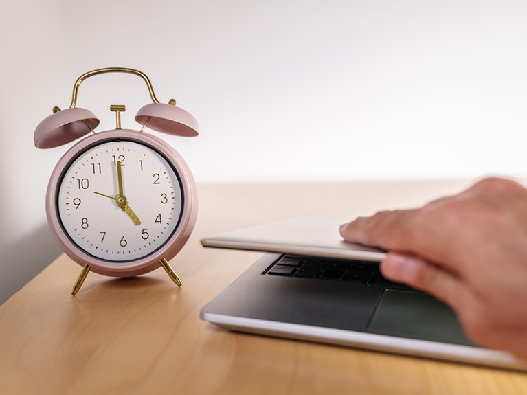 Clock marking 5 pm and a laptop with the lid closed.