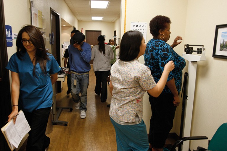 Busy medical clinic with staff and patients walking up and down a corridor. A woman is being weighed.