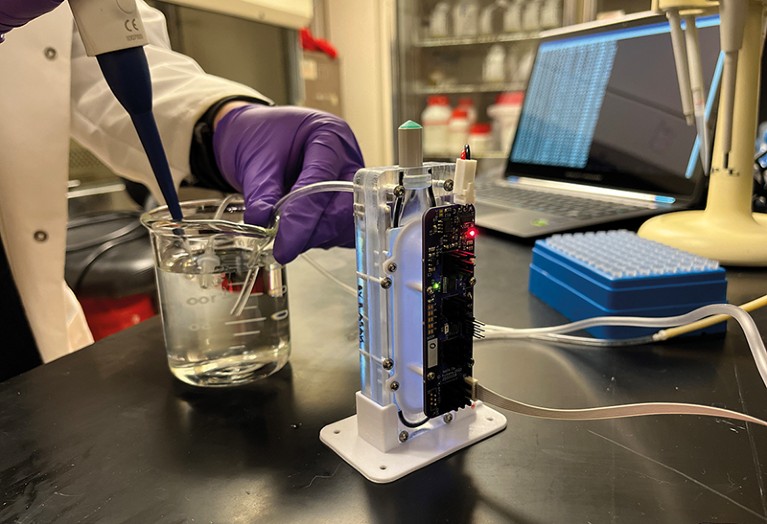 A glass jar filled with clear liquid connected by tubes to a small, upright device with red and green lights.