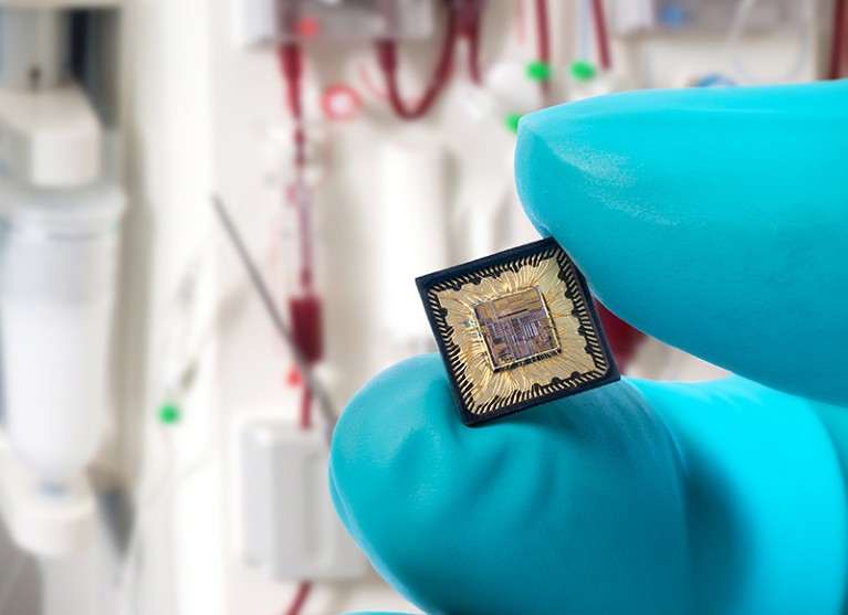 Close-up of a microchip held by a blue-gloved hand in a lab setting.