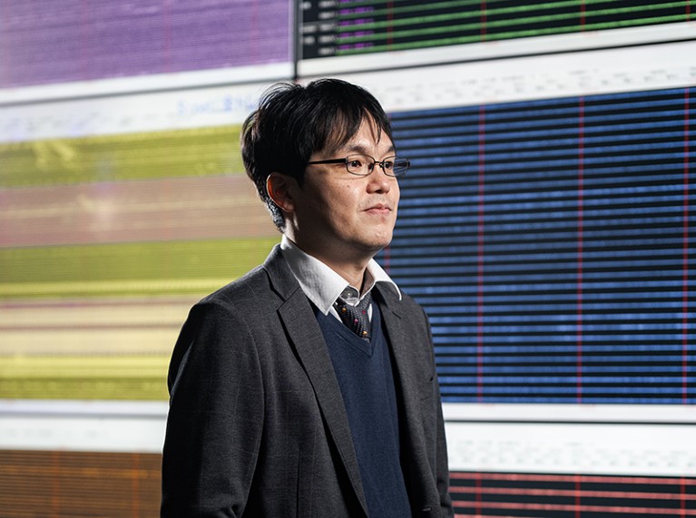 Tatsuya Kubota standing in front of large monitoring system with several display screens