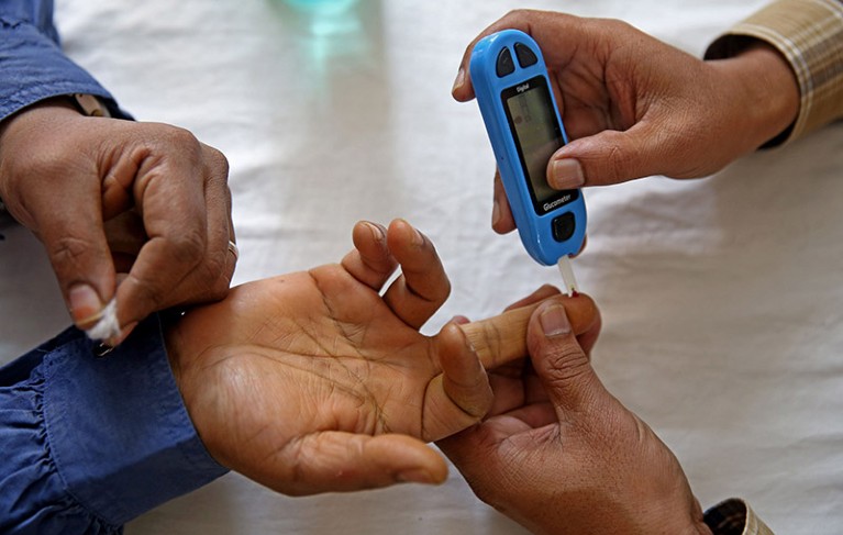 A close up view of the hands of a health worker and a man undergoing a Gluco meter random blood sugar test.